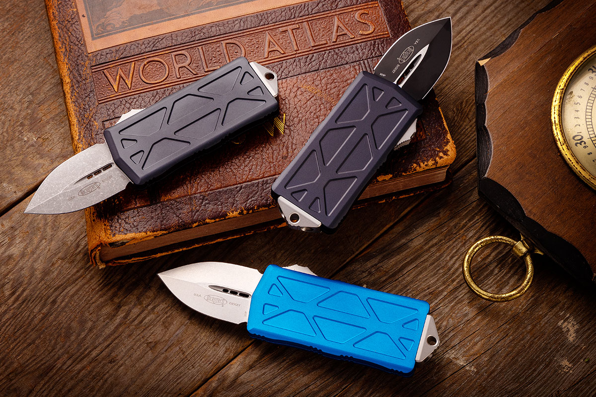 Collection of Microtech Exocet knives sitting on a vintage, leather-bound atlas