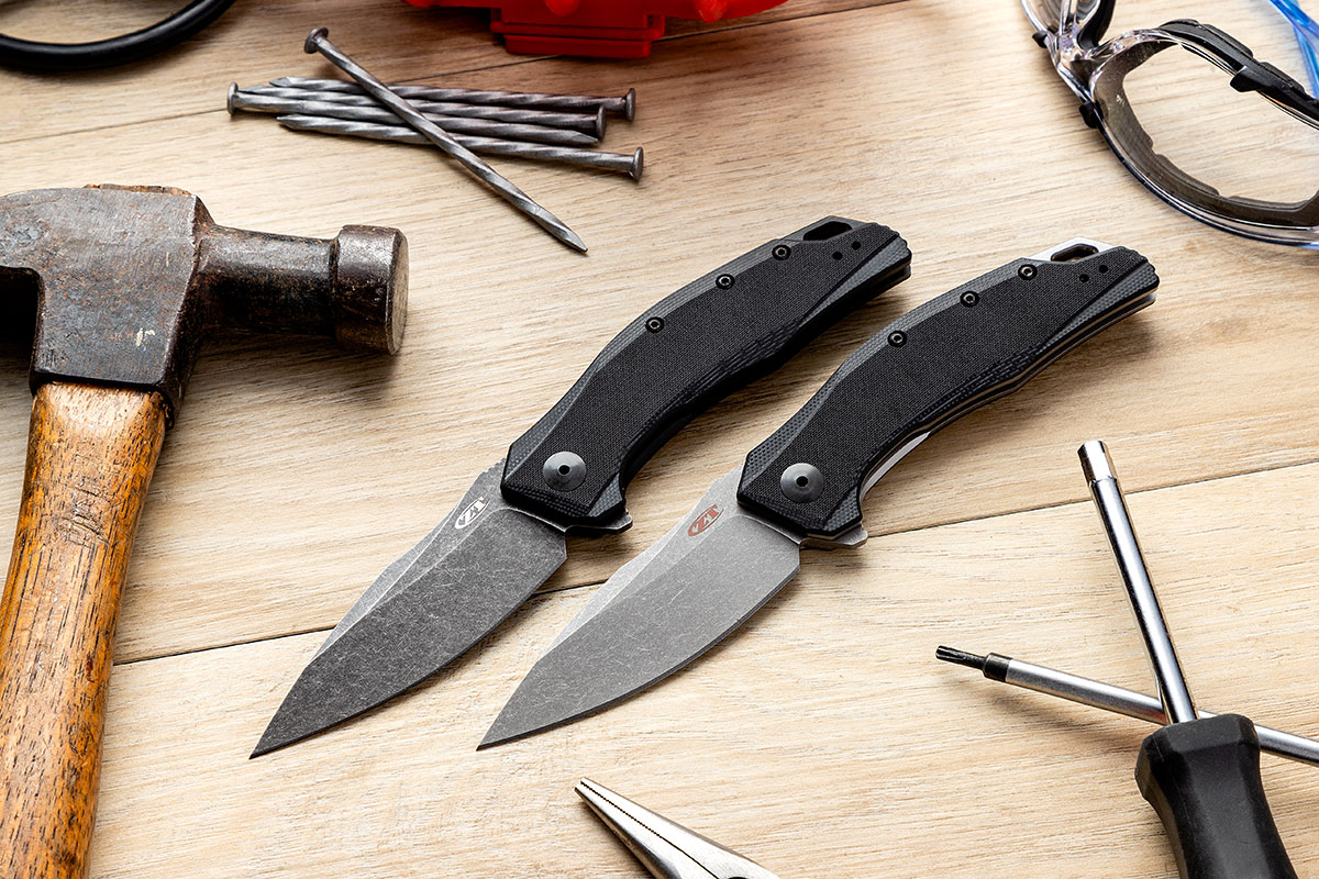 A ZT0357 and ZT0357BW knife among a collection of tools and hardware including hammer, pliers, safety goggles, screwdriver, and nails.