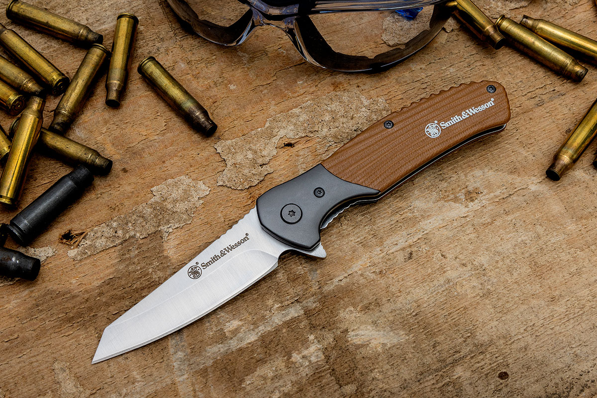 Smith & Wesson Stave knife on a wood surface surrounded by bullet casings and safety goggles