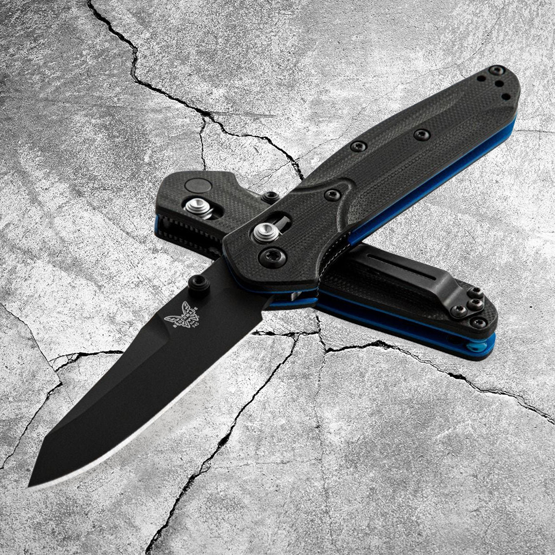 two black Benchmade Osborne folding knives, one sitting open perpendicular over one folded, on a stone background