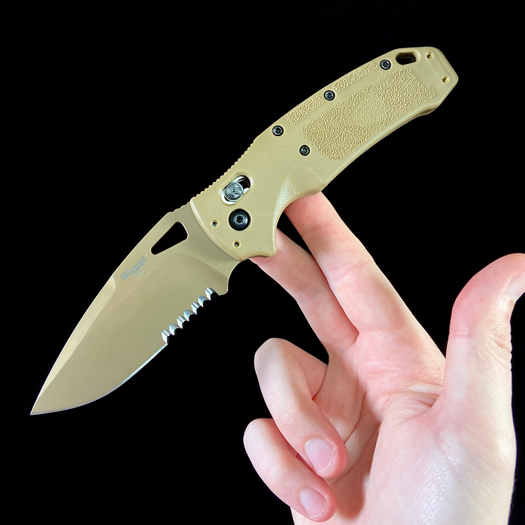 an open Hogue K320 folding knife balanced on two fingers with a black background.