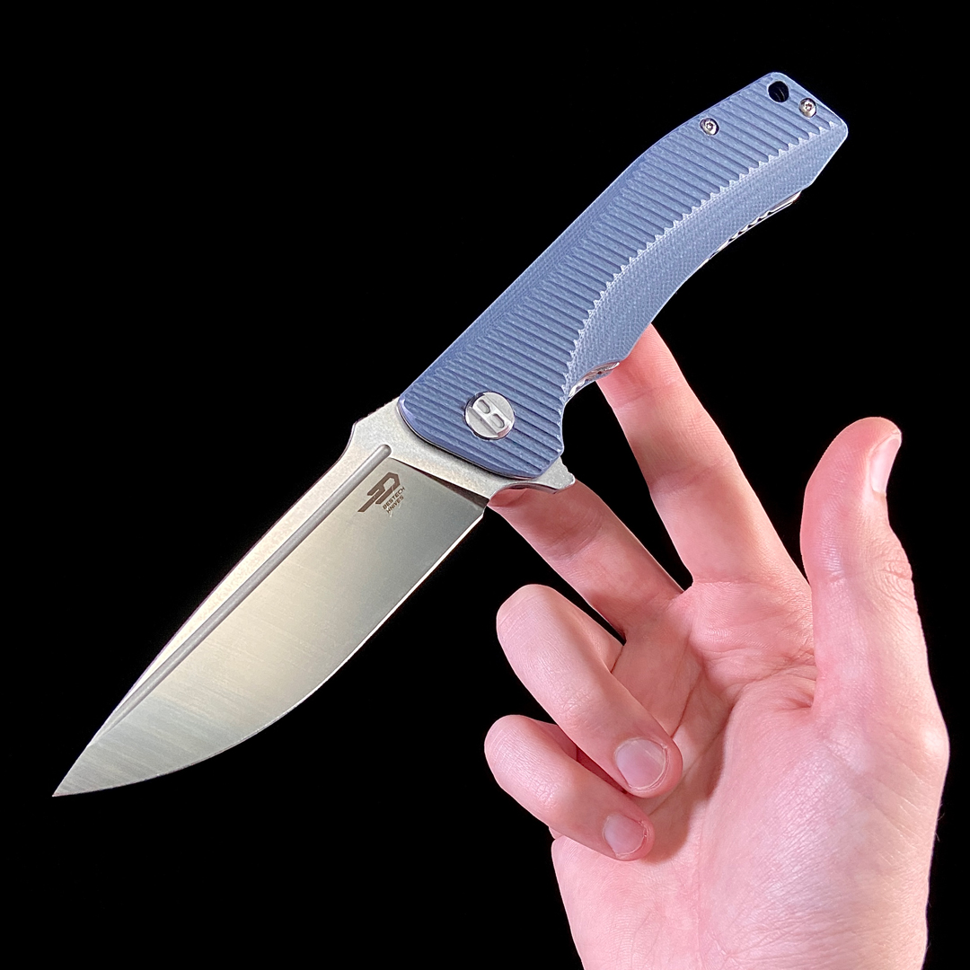 An open Bestech Mako with Milled Gray and Blue G10 Handles, balanced on two fingers on a black background