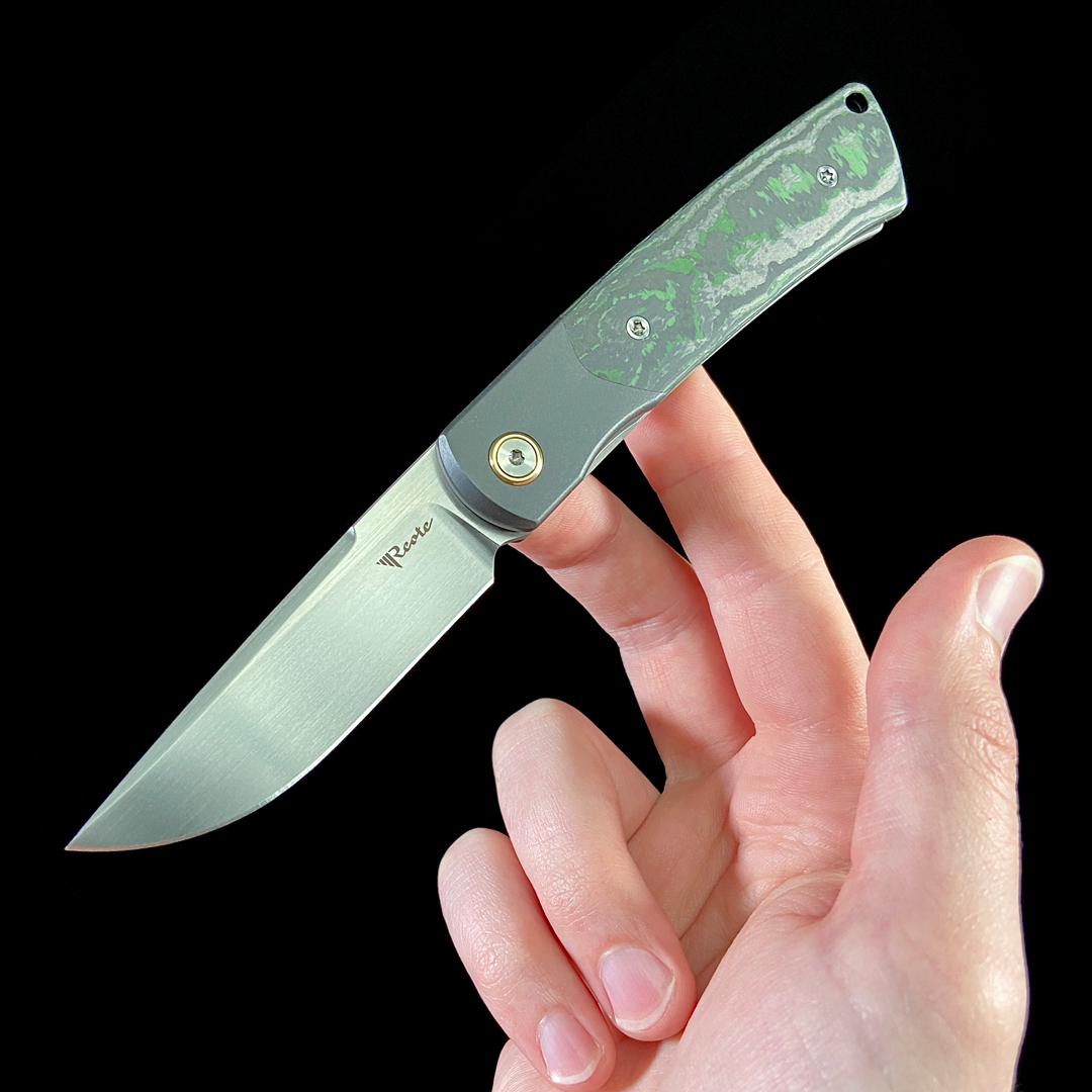 Reate Tribute folding knife, open in hand, black background