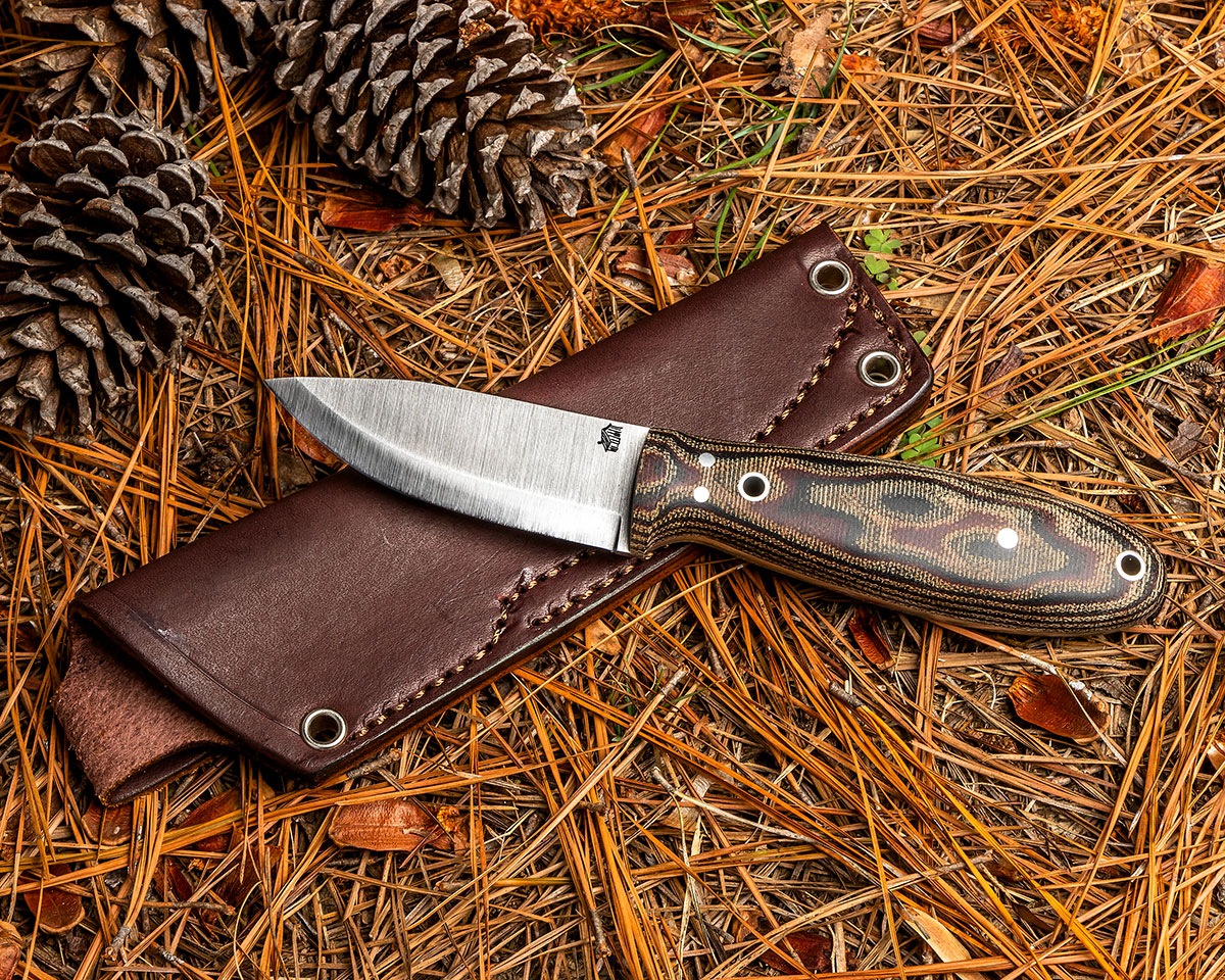 L.T. Wright Holy Bushman V2 resting on leather sheath among pine needles