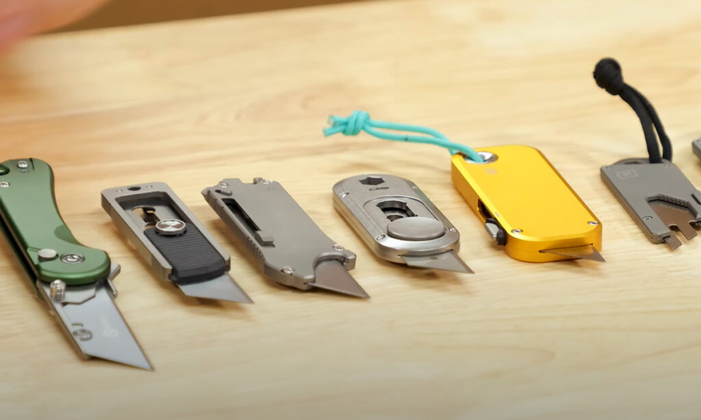 Six EDC utility knives arranged in a line on a table